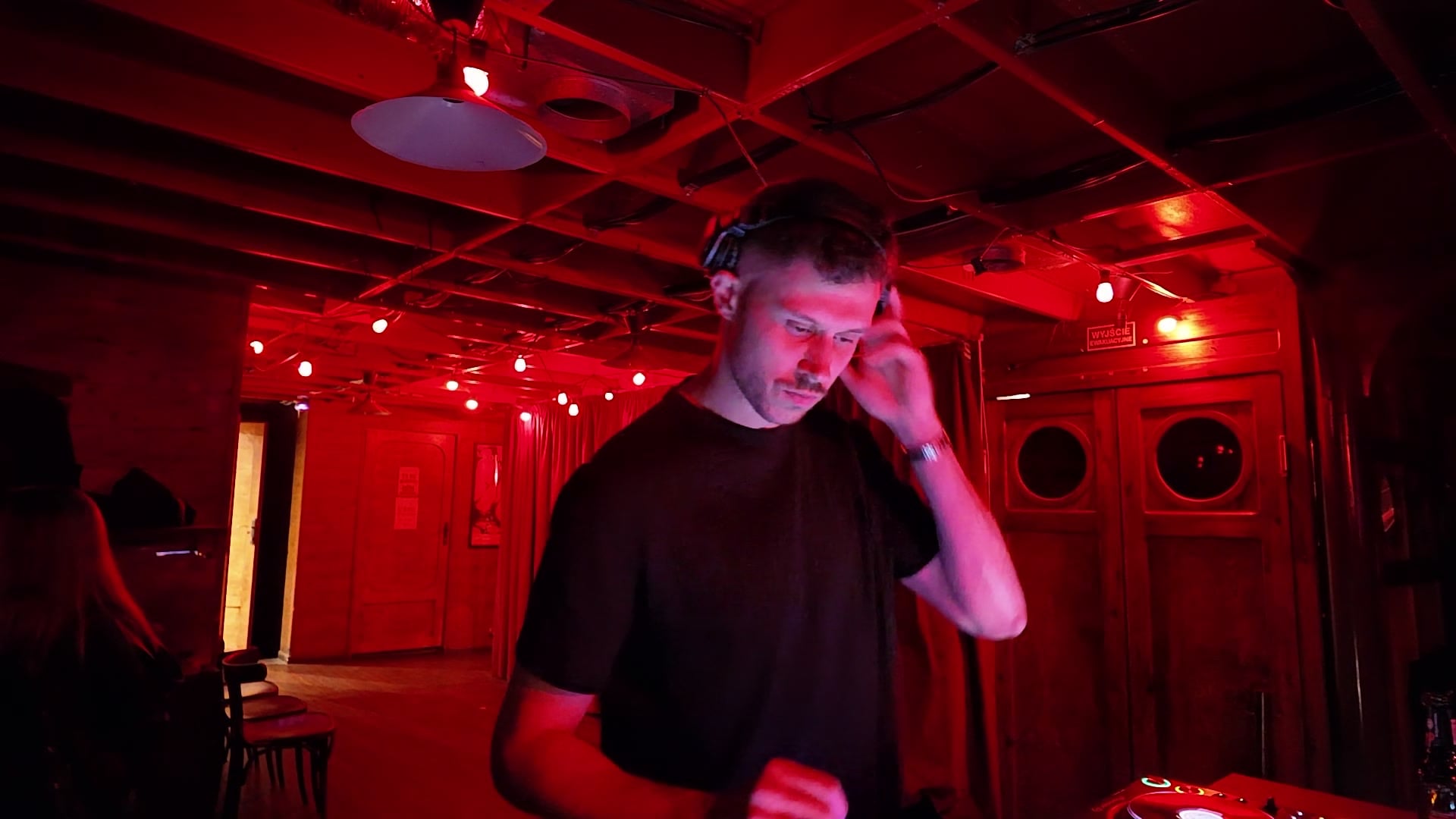 Bartek za konsoletą DJ w czerwonym świetle, ręka przy słuchawce